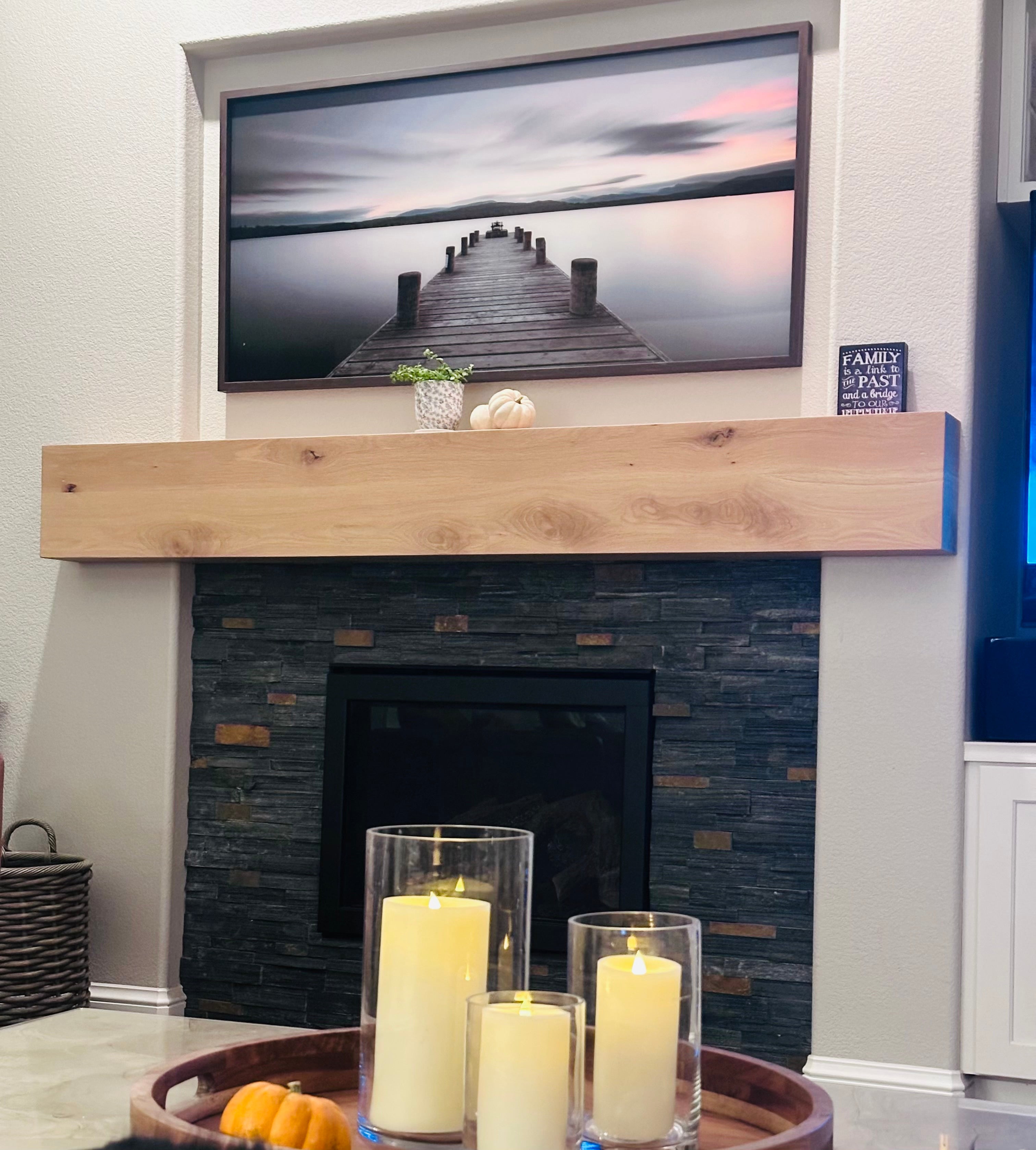 Fireplace with wooden mantel, candles, and a television displaying a dock scene.